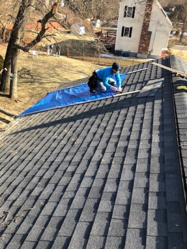 Roofer covering damaged roof for an emergency roof repair