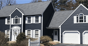 A photo of a large, navy-colored home with white accents displaying its new roof