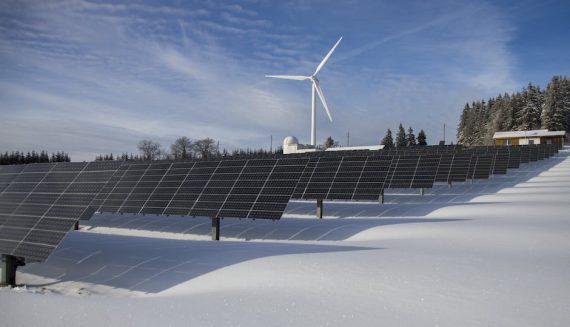 A row of solar panels and a wind turbine in after it has freshly snowed