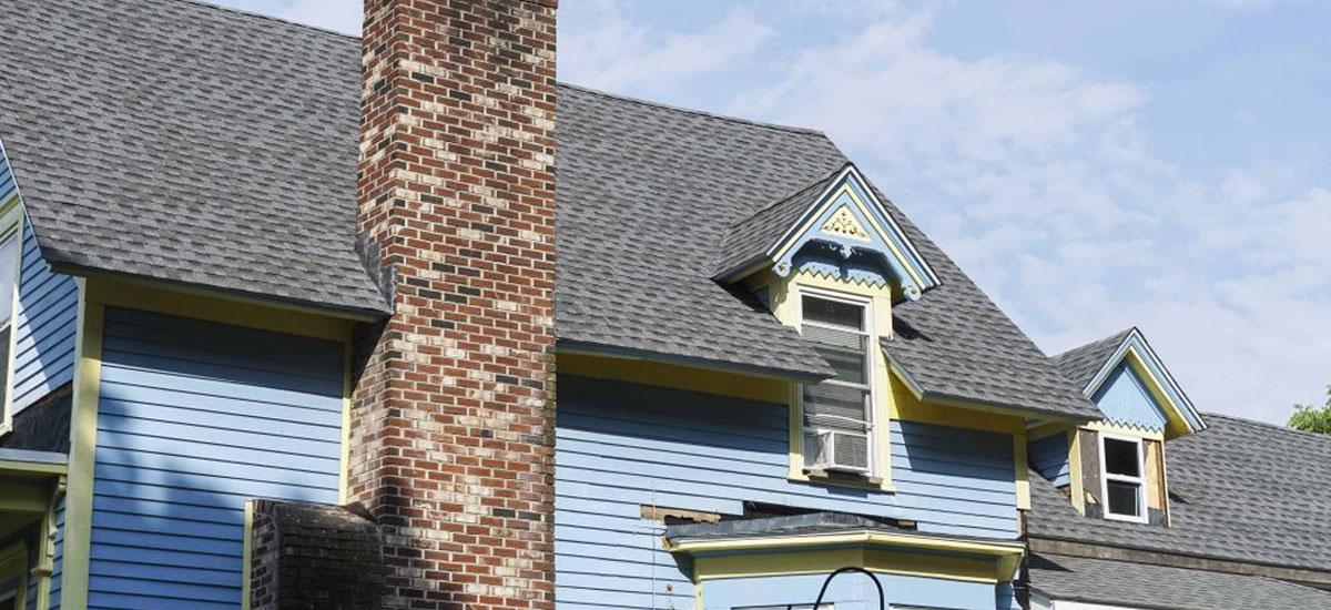 01-how-long-does-a-roof-last Up-close view of an asphalt roof on an older blue home
